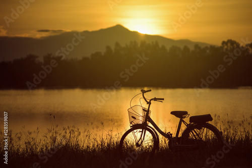 retro vintage bicycle near the lake at sunset moment. silhouette bicycle at the sunset with grass field.big mountain and sunset background.journey concept.lonely concept