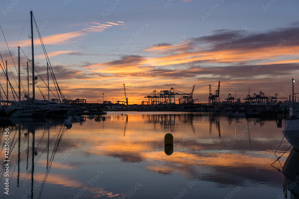 Twilight at Valencia harbor sunrises docked sailboats and cargo port cranes red colors in the sky and water reflection