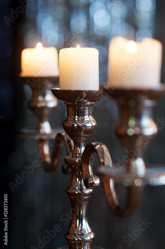 silver candlestick with three burning white candles on dark background