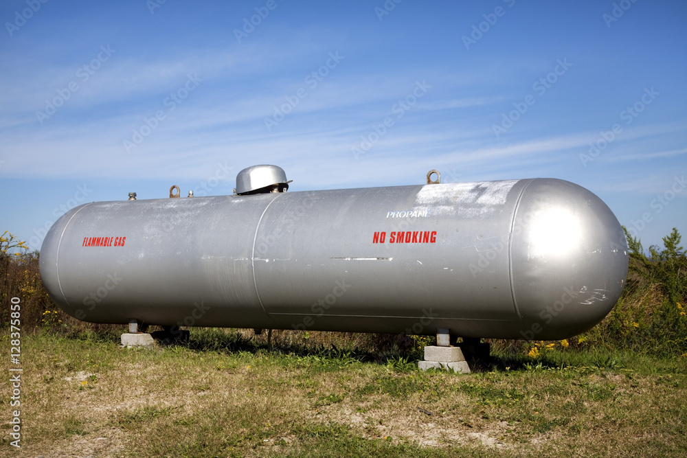Shiny silver propane tank in field under blue sky. Horizontal. Shiny silver propane tank in field under blue sky. Horizontal.