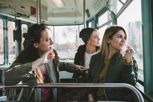 Three beautiful young women sitting in tram and looking through window.