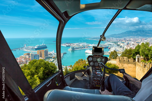 Helicopter cockpit flies in port of Malaga from the Gibralfaro Castle, Andalusia, Spain, with pilot arm and control board inside the cabin.