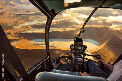 Helicopter cockpit flies in Deadvlei, Sossusvlei desert in Namib Naukluft National Park, Namibia, with pilot arm and control board inside the cabin.