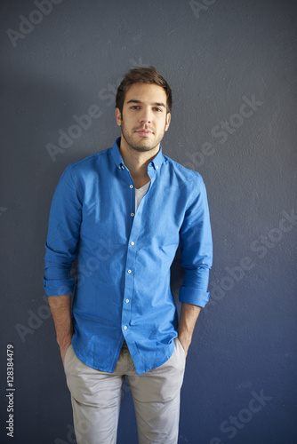 Young man portrait with copy space. Shot of a handsome man relaxing in front of a grey wall while looking at camera and smiling. 
