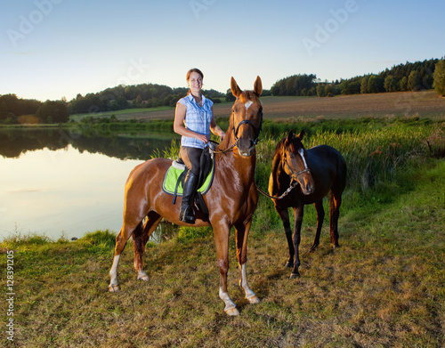 Woman with Two Horses by a Lake at Sunset