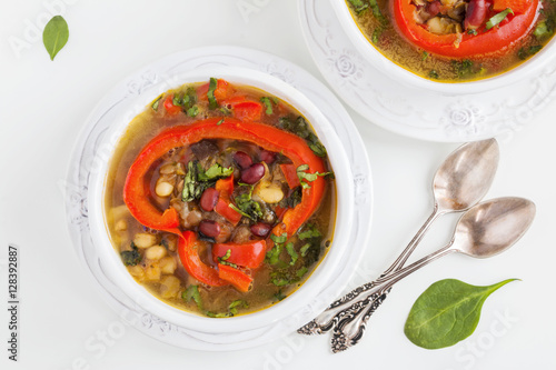 Spiced vegan kidney bean and lentil thick soup with tomatoes and bell pepper. Vintage ceramic bowl on white table, top view.