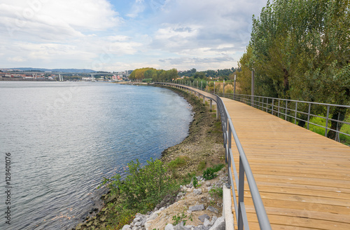 River lake water pier wooden catwalk bank way path cycling track urban park city horizon background © matousekfoto