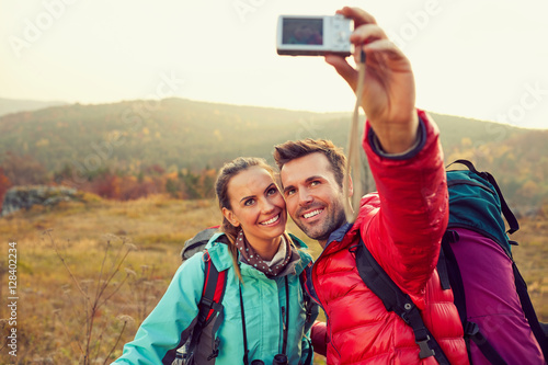 Happy couple taking selfie with camera during autumn hike with backpacks