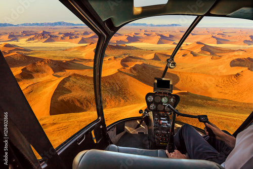 Helicopter cockpit flies in Dead Valley, Sossusvlei desert in Namib Naukluft National Park, Namibia, with pilot arm and control board inside the cabin.