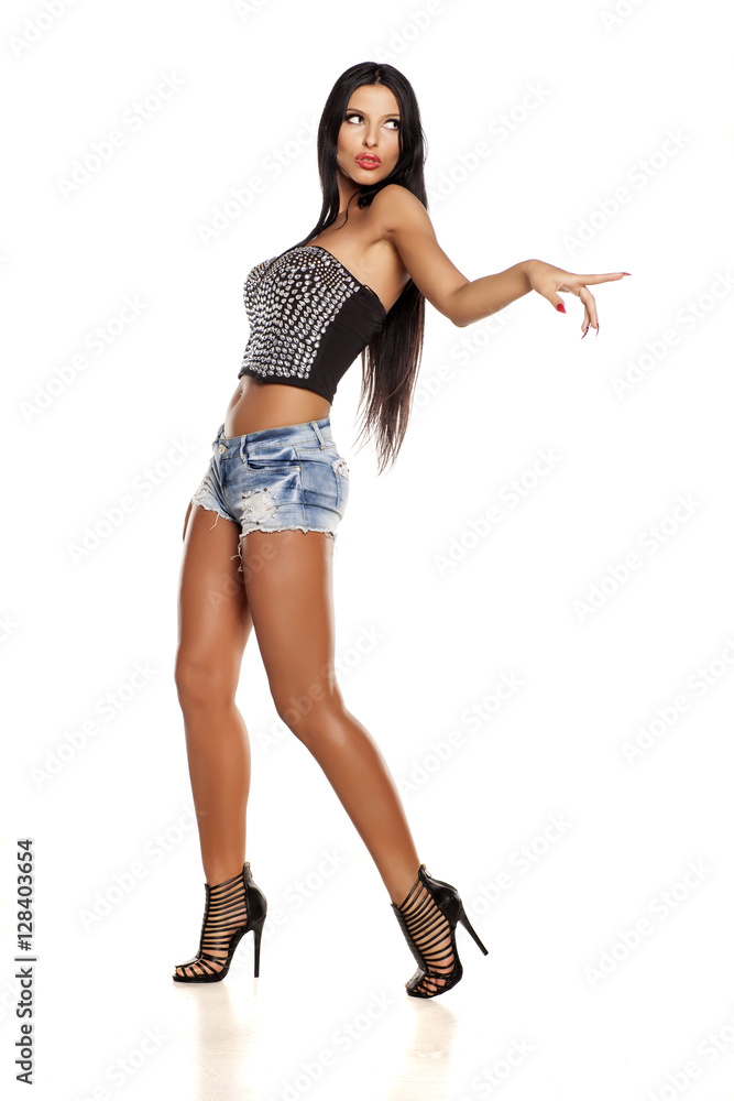 attractive young woman in short jeans pointing on a white background attractive young woman in short jeans pointing on a white background