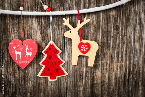 Red Christmas decorations hanging on branch over wooden background