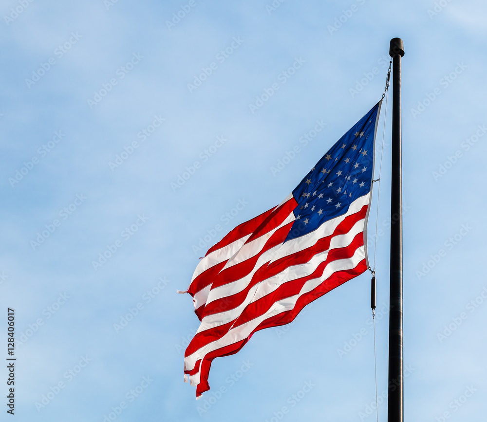 Obraz premium American flag flying on from a black flagpole against a cool blue sky.