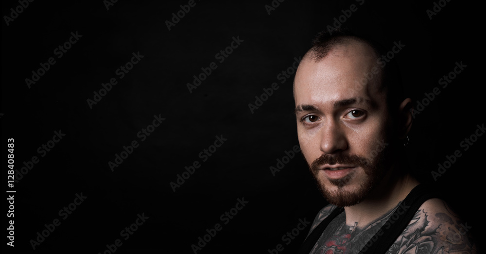 Handsome close up portrait of european serious guy with short beard on neutral black background. A little smirk on the brutal face. Copy space for advertising or sale text.