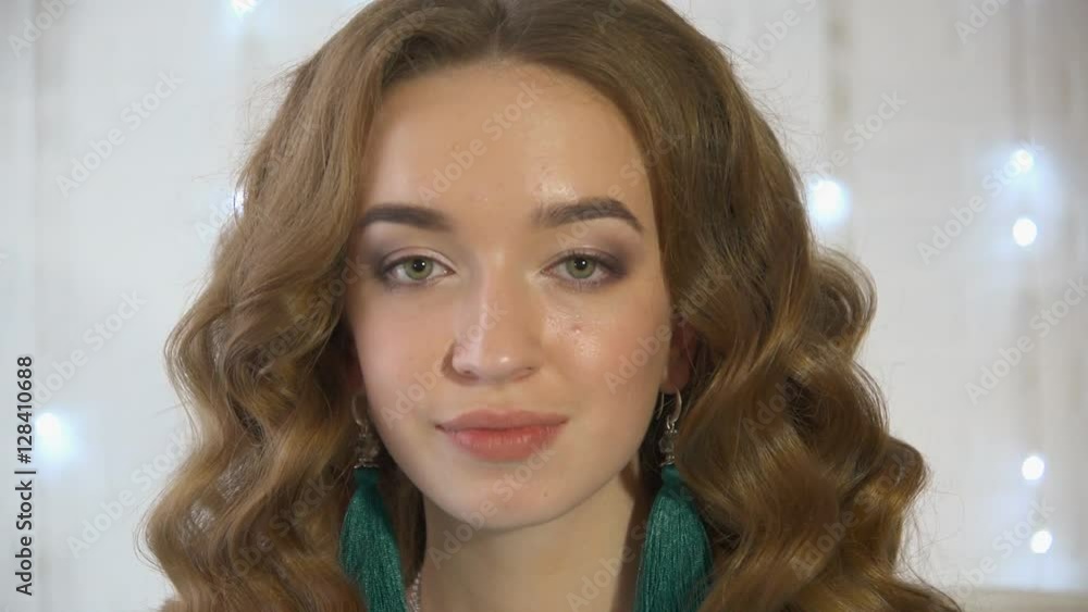 Brunette woman in a turquoise dress sitting on a luxury sofa near white brick wall decorated with garland. A festive portrait of a girl with loose hair with a christmas light bulbs. Brunette woman in a turquoise dress sitting on a luxury sofa near white brick wall decorated with garland. A festive portrait of a girl with loose hair with a christmas light bulbs.
