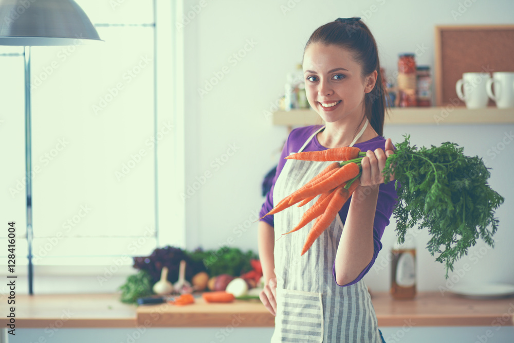 Happy young woman holding bunch of carrots in kitchen