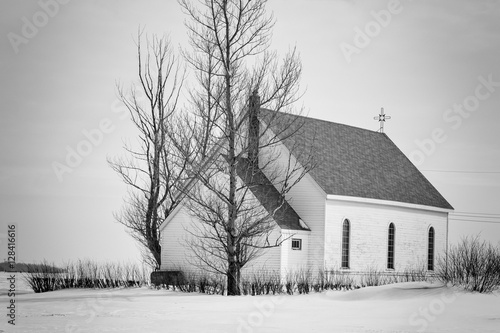 Slika na platnu horizontal black and white image of an old rustic white wooden church sitting on a blanket of snow in the winter time