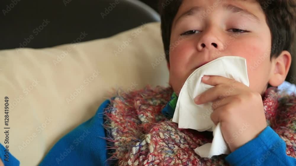 Tired boy at home sick with flu lying on bed with thermometer in mouth resting. Blows his nose in a paper handkerchief Tired boy at home sick with flu lying on bed with thermometer in mouth resting. Blows his nose in a paper handkerchief