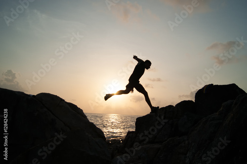 Man jump through the gap between hill.man jumping over cliff on sunset background,Business concept idea