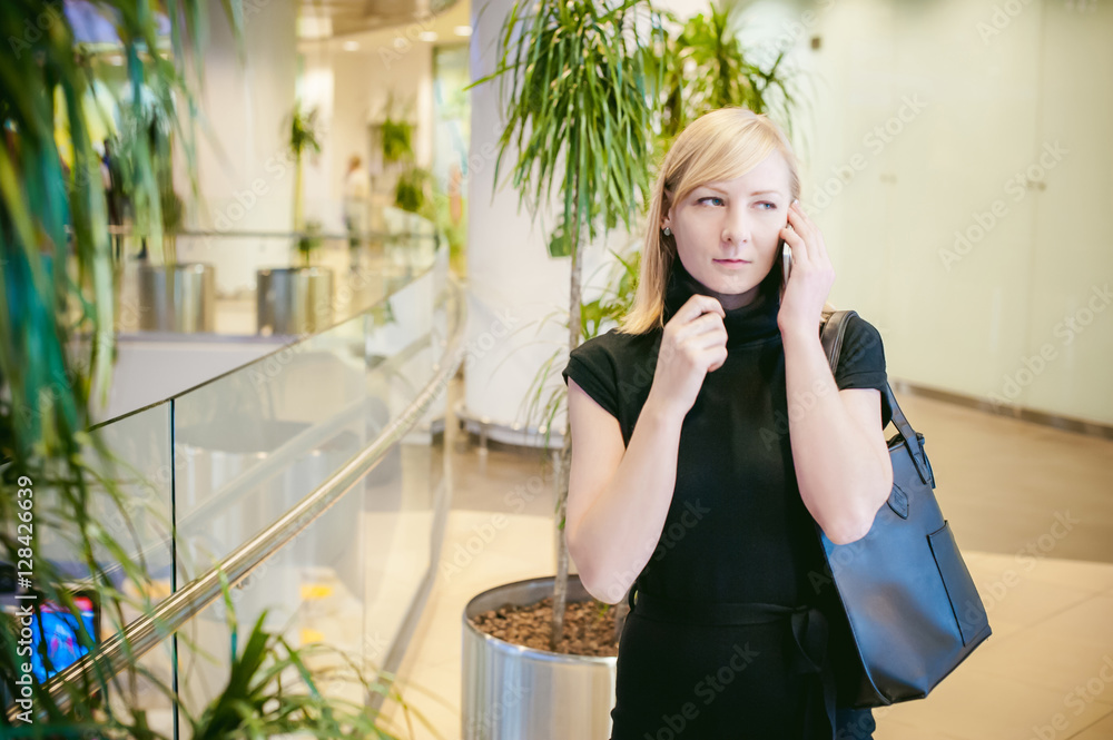 Girl and telephone. blonde in a black dress holding a phone. business talks on mobile phone in business centers. on the background of palm trees Girl and telephone. blonde in a black dress holding a phone. business talks on mobile phone in business centers. on the background of palm trees