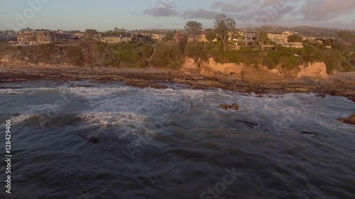 Aerial panning aerial looking toward the beaches and cliff side homes in the Corona Del Mar Neighborhood of Newport Beach, California, during sunset, and wind driven surf during a winter weekend