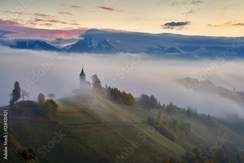 In the morning mist, St. Primoz church near Jamnik at dusk with alps in background, Slovenia photo