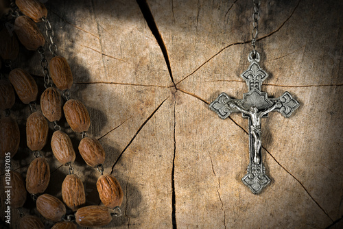 Silver crucifix and a rosary with wooden beads on a tree trunk