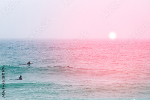 Two surfers floating on the boards lying in the ocean at sunset.