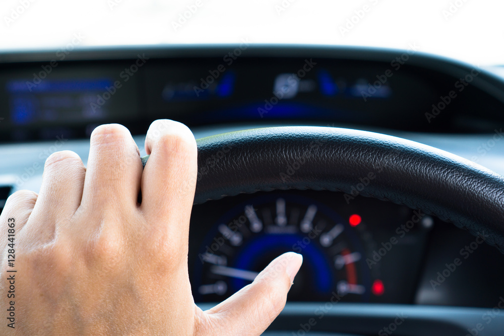 Hand holding steering wheel in the car with gauge and speedometer in blur background 
