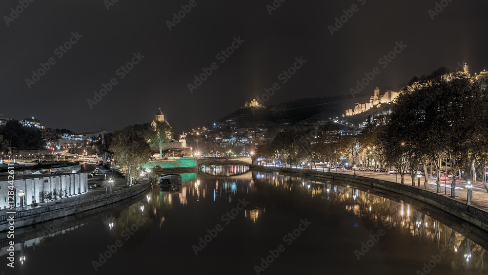 Fototapeta premium Georgia, Tbilisi - November 23, 2016. The lights of the city at night and reflection in the Kura River, Assumption Church Metekhi, Narikala fortress and the movement of vehicles on the street