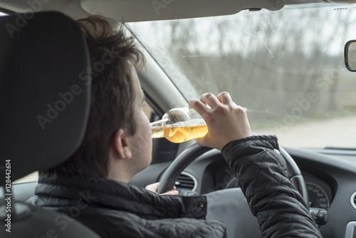 Young man driving his car while drinking alcohol