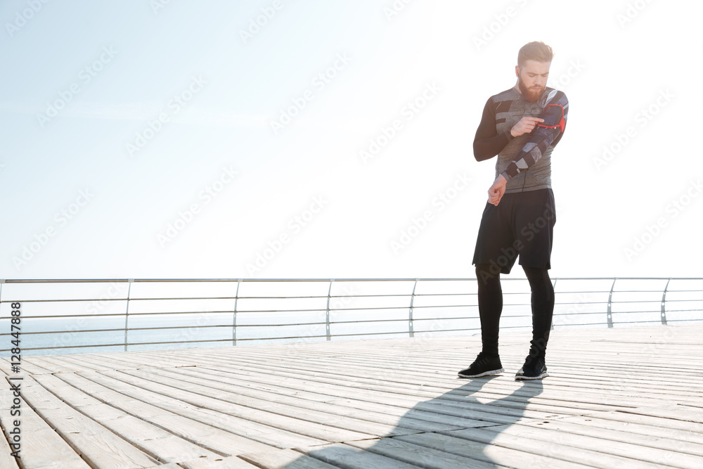 Full length runner near the sea looking at phone Full length runner near the sea looking at phone