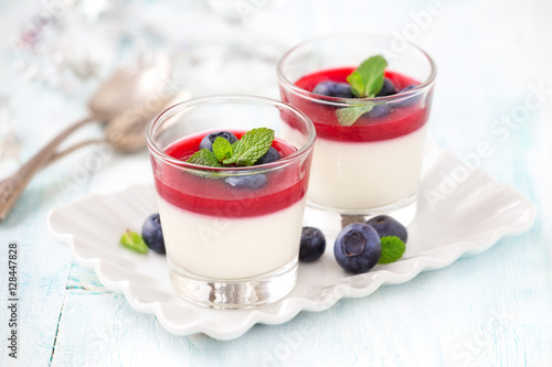 Delicious Italian dessert Panna Cotta with raspberry coulis and fresh blueberries served for two in small transparent glasses photo
