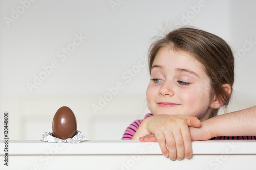 Принти на полотні Little girl with an impish smile looking at the chocolate egg