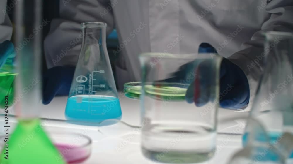 Tracking closeup shot of hands of chemists working with chemicals in flasks and tubes at laboratory table Tracking closeup shot of hands of chemists working with chemicals in flasks and tubes at laboratory table