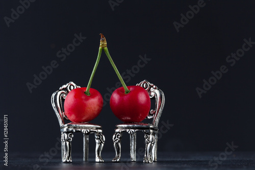 Couple of red cherries placed on beautiful silver chairs on black background with copy space. Relationship concept.