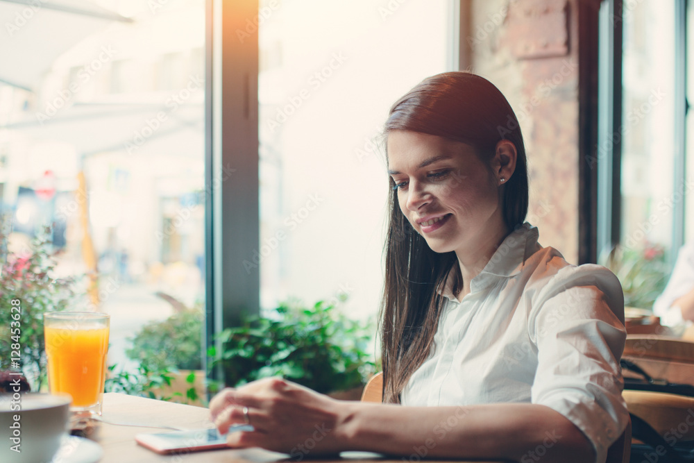 Handsome smiling woman sitting in cafe and using mobile phone to type new letter while having breakfast Handsome smiling woman sitting in cafe and using mobile phone to type new letter while having breakfast