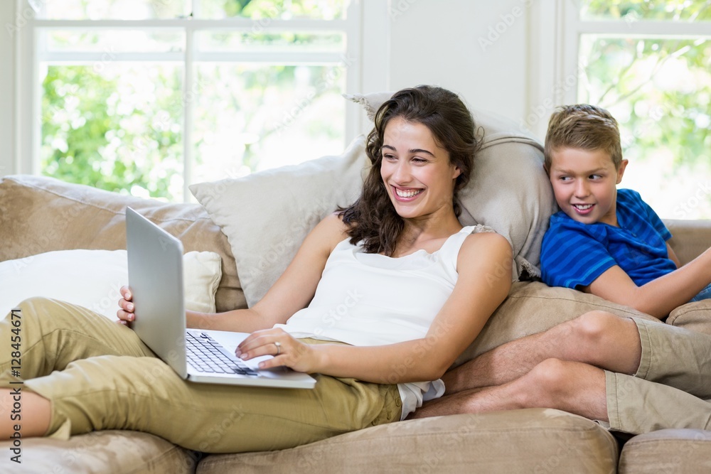 Mother and son sitting on sofa and using laptop