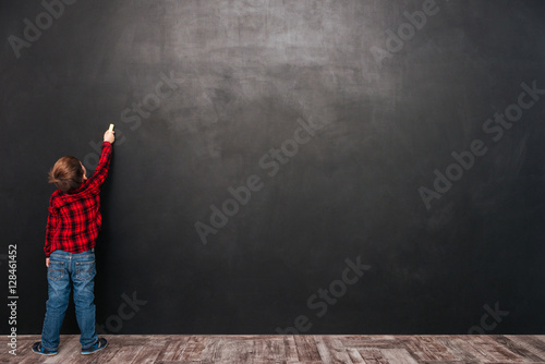 Pretty child standing near blackboard and drawing on it