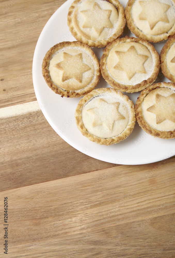 A plate full of freshly baked mince pies on a wooden kitchen counter background with blank space below