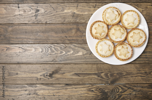 A plate full of freshly baked mince pies on a rustic wooden table top background with empty space at side