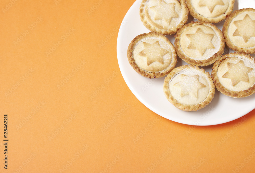 A plate full of freshly baked pies on a bright orange background with a blank space at side