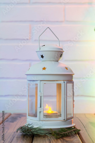 Christmas Decorations with lamp with candle, fir branch on wooden table against brick background