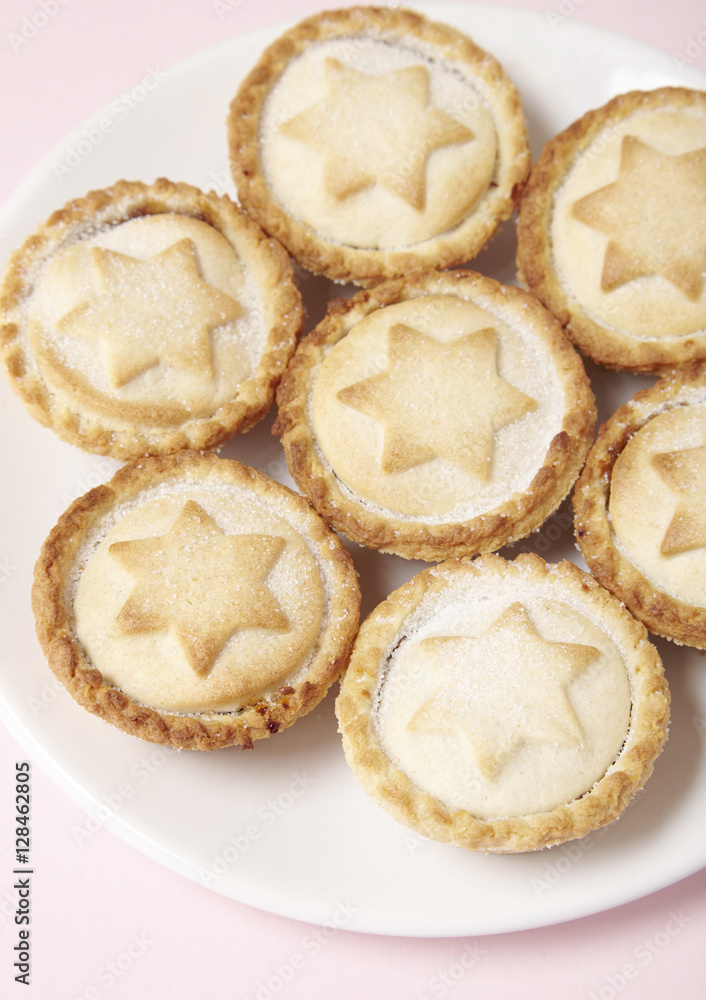 Close up of a plate full of freshly baked fruit pies on a pastel pink background