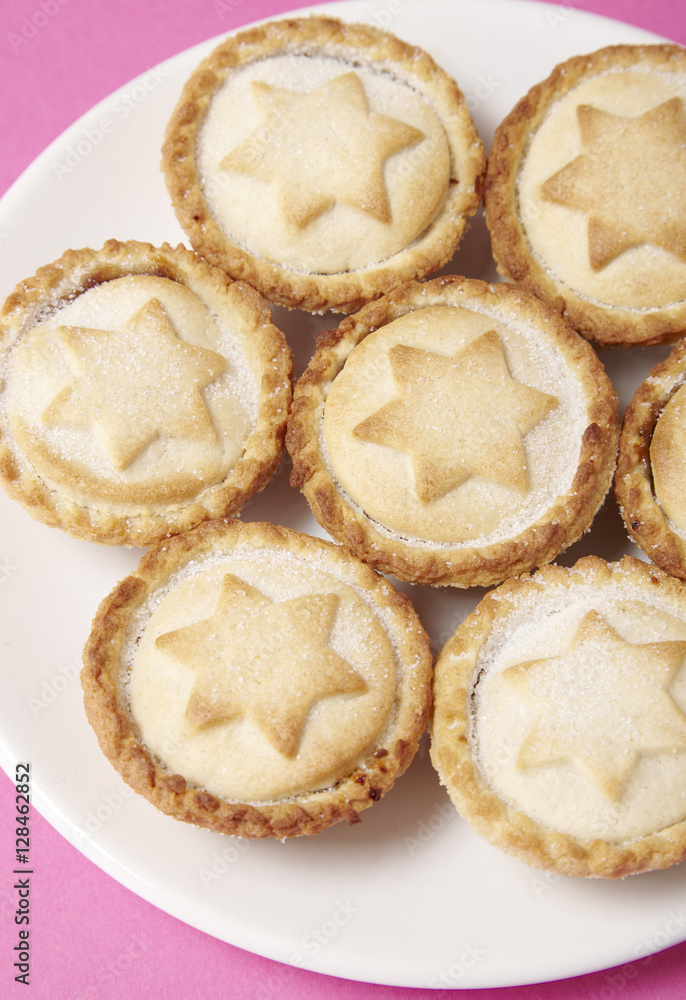 A close up of a plate full of freshly baked mince pies on a bright pink background