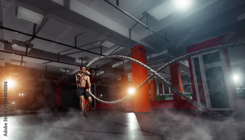 Fitness man working out with battle ropes at a gym - obrazy, fototapety, plakaty 