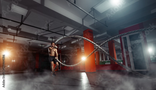 Fitness man working out with battle ropes at a gym
