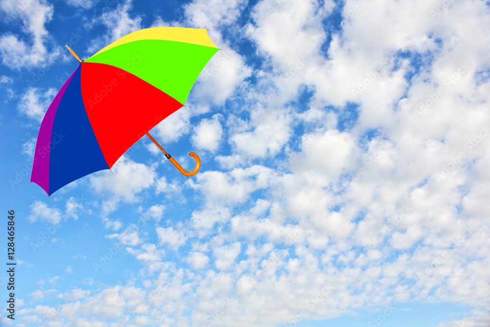 Multicolored umbrella flies in sky against of pure white clouds.Wind of change concept.