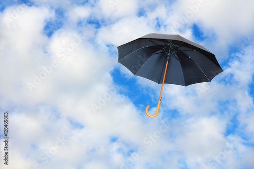 Mary Poppins umbrella.Black umbrella flies in sky against of pure white clouds.Wind of change concept.