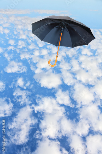 Black umbrella flies in sky against of white clouds.Mary Poppins Umbrella..Wind of change concept.