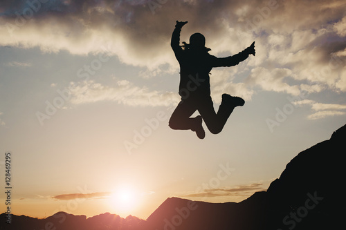 Silhouette of a beautiful hiker girl jumping over sunset